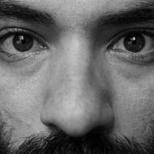 Macro black and white close-up of a man's nose and eyes as he performs a sniff test for scent dispersal near a harvest transport truck.